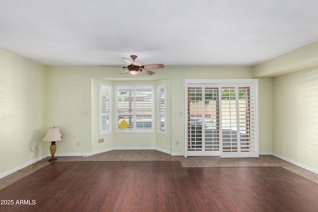 unfurnished room featuring dark wood-style floors, a ceiling fan, and baseboards