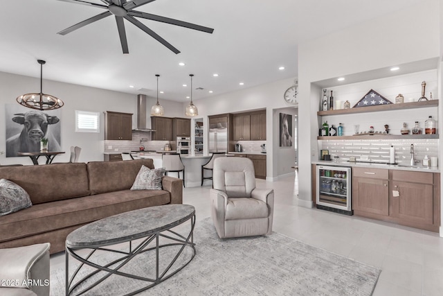 living room featuring ceiling fan with notable chandelier, wet bar, light tile patterned floors, and wine cooler