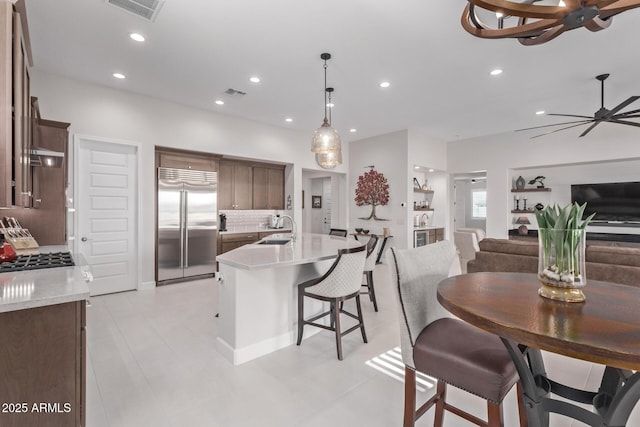 kitchen with ceiling fan, sink, hanging light fixtures, built in fridge, and a kitchen island with sink