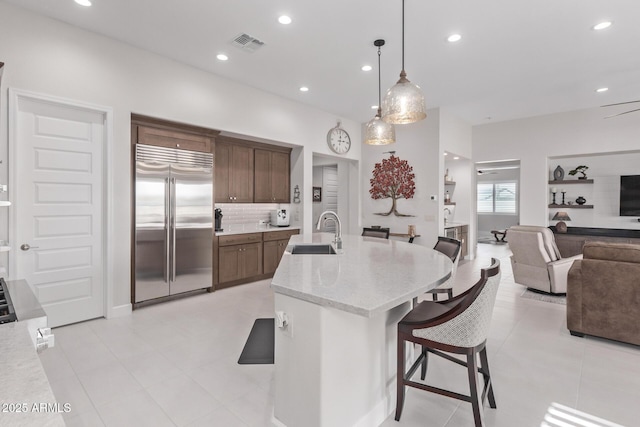 kitchen with a breakfast bar, sink, stainless steel built in refrigerator, pendant lighting, and dark brown cabinets