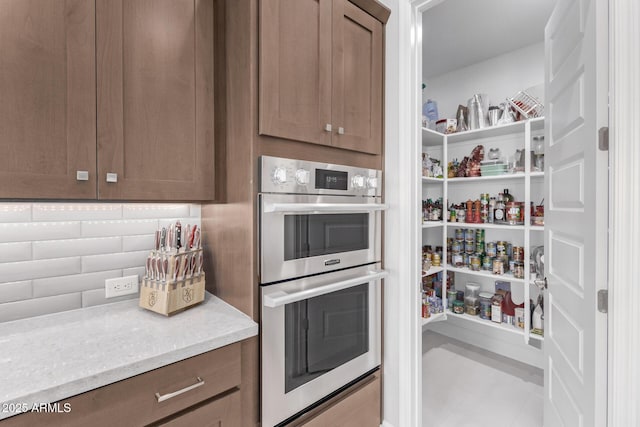 kitchen featuring double oven, backsplash, and light stone counters