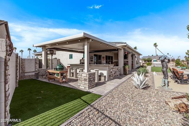 rear view of property featuring an outdoor kitchen, a patio area, and exterior bar