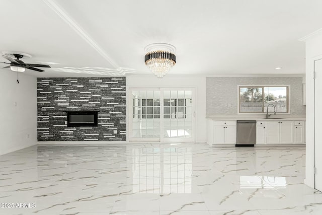 unfurnished living room with a tiled fireplace, ornamental molding, sink, and ceiling fan with notable chandelier