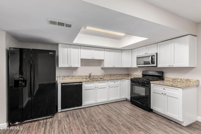 kitchen featuring a tray ceiling, sink, black appliances, light hardwood / wood-style flooring, and white cabinets