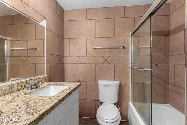 full bathroom featuring combined bath / shower with glass door, vanity, toilet, and tile walls