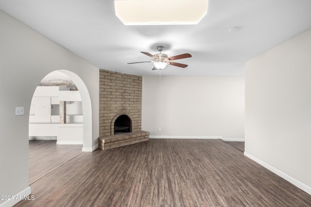 unfurnished living room featuring ceiling fan, dark wood-type flooring, and a brick fireplace