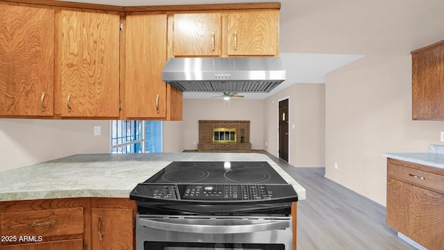 kitchen featuring light wood finished floors, stainless steel electric stove, extractor fan, light countertops, and a brick fireplace