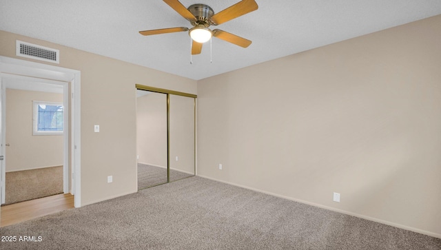 unfurnished bedroom featuring ceiling fan, a closet, visible vents, and light colored carpet