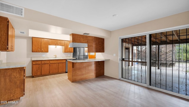 kitchen featuring brown cabinets, light countertops, visible vents, light wood-style flooring, and a peninsula