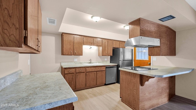 kitchen with under cabinet range hood, stainless steel appliances, a peninsula, light wood-type flooring, and brown cabinetry