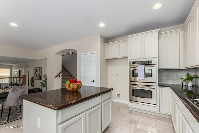 kitchen with white cabinetry, tasteful backsplash, stainless steel double oven, dark stone counters, and a center island