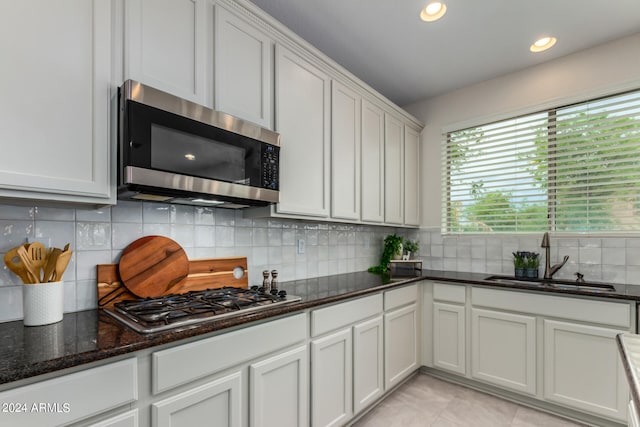 kitchen with appliances with stainless steel finishes, tasteful backsplash, sink, white cabinets, and light tile patterned floors