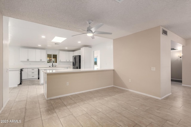 kitchen featuring stainless steel fridge, ceiling fan, a skylight, white cabinets, and kitchen peninsula