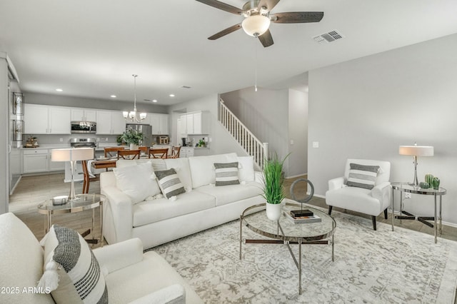 living area featuring recessed lighting, visible vents, stairway, light wood-style floors, and ceiling fan with notable chandelier