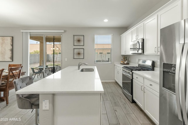 kitchen with a center island with sink, appliances with stainless steel finishes, a sink, wood tiled floor, and a wealth of natural light