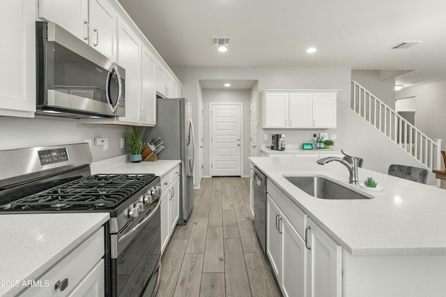 kitchen featuring wood finish floors, a sink, visible vents, appliances with stainless steel finishes, and an island with sink