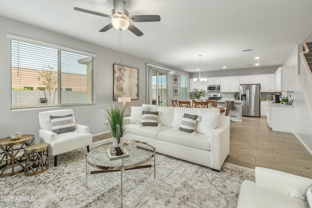 living area featuring recessed lighting, ceiling fan with notable chandelier, visible vents, baseboards, and light wood finished floors