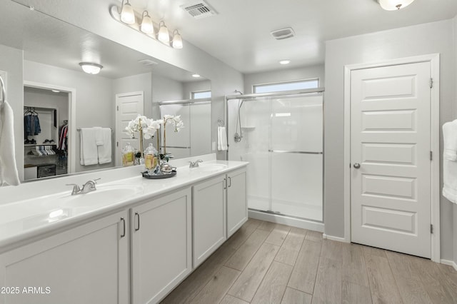 full bathroom with double vanity, a stall shower, visible vents, wood finished floors, and a sink