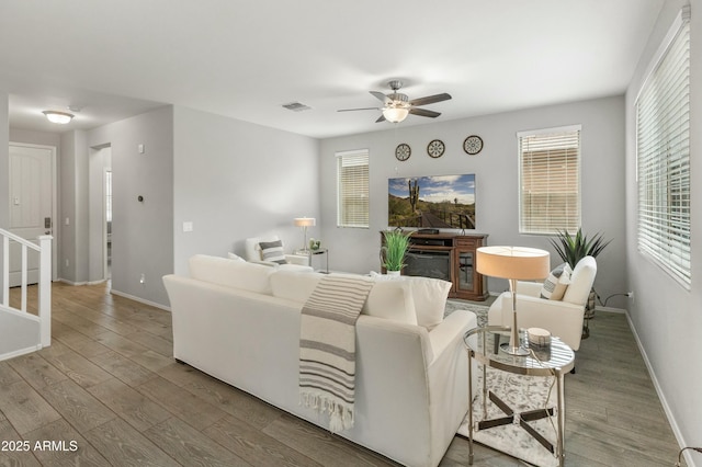 living area with a ceiling fan, a fireplace, baseboards, and wood finished floors