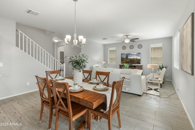 dining room featuring light wood finished floors, visible vents, stairway, baseboards, and ceiling fan with notable chandelier