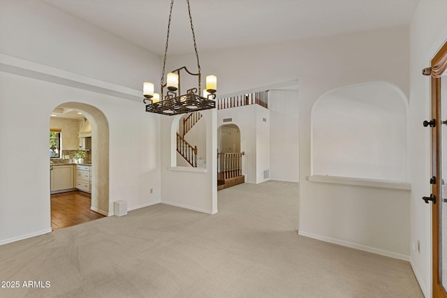 unfurnished dining area featuring carpet floors, stairway, baseboards, and arched walkways