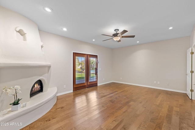 unfurnished living room featuring a warm lit fireplace, baseboards, wood finished floors, and recessed lighting