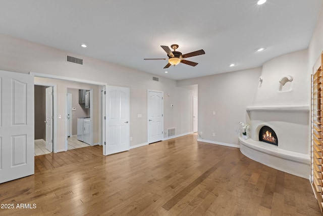 unfurnished living room featuring a lit fireplace, wood finished floors, visible vents, and a ceiling fan