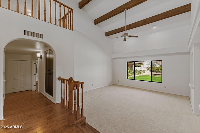 empty room featuring baseboards, visible vents, arched walkways, high vaulted ceiling, and beam ceiling