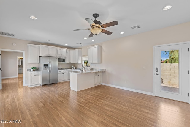 kitchen with stainless steel appliances, visible vents, white cabinets, light wood-type flooring, and a peninsula