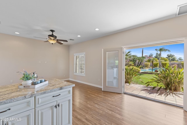 kitchen with light wood-style flooring, recessed lighting, visible vents, baseboards, and light stone countertops