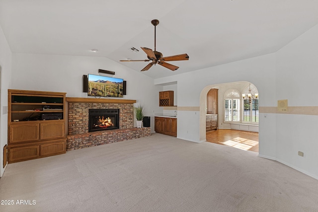 unfurnished living room featuring arched walkways, a fireplace, lofted ceiling, carpet flooring, and ceiling fan