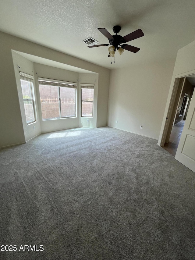 carpeted empty room with visible vents, a textured ceiling, a wealth of natural light, and a ceiling fan