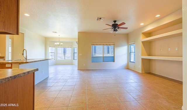 kitchen featuring visible vents, brown cabinetry, decorative light fixtures, a textured ceiling, and a sink