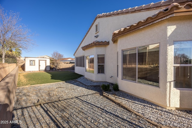 back of property featuring an outbuilding, a fenced backyard, a tiled roof, a lawn, and stucco siding