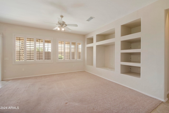 spare room with built in shelves, ceiling fan, and light colored carpet