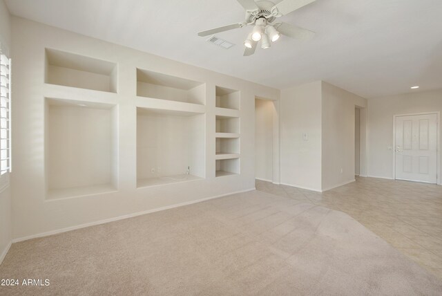 unfurnished room featuring built in shelves, light carpet, and ceiling fan