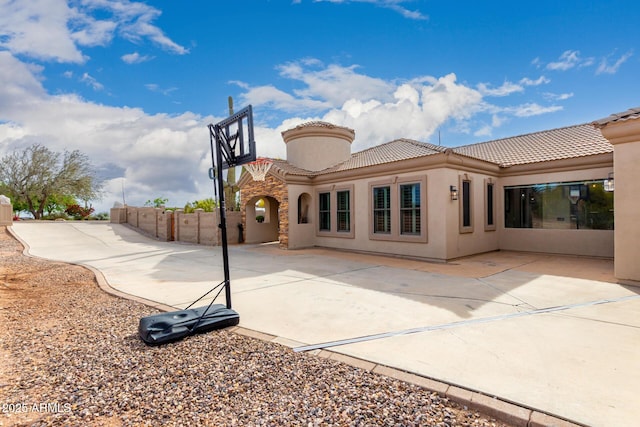 rear view of property featuring stucco siding, a tile roof, and fence