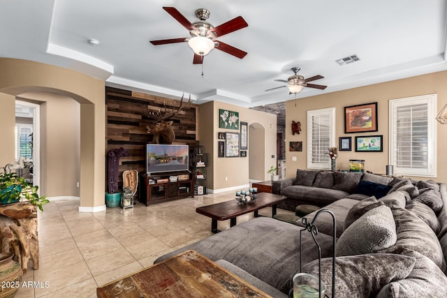 living room with visible vents, a ceiling fan, baseboards, arched walkways, and light tile patterned floors