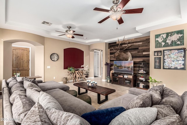 living area with ceiling fan, visible vents, arched walkways, light tile patterned floors, and a tray ceiling