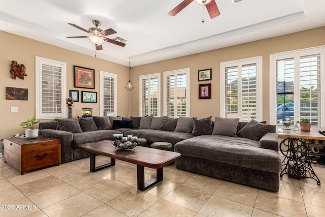 living area featuring light tile patterned flooring, ceiling fan, and a raised ceiling