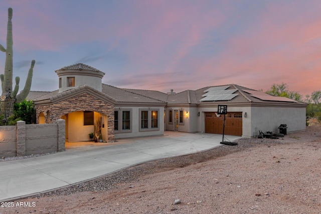 back of property featuring fence, a garage, solar panels, a tiled roof, and driveway