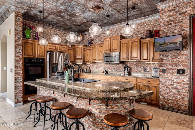 kitchen featuring a breakfast bar area, backsplash, brown cabinetry, light tile patterned floors, and black appliances