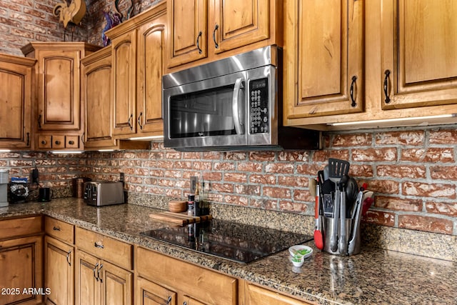 kitchen with brown cabinetry, stainless steel microwave, black electric stovetop, and tasteful backsplash