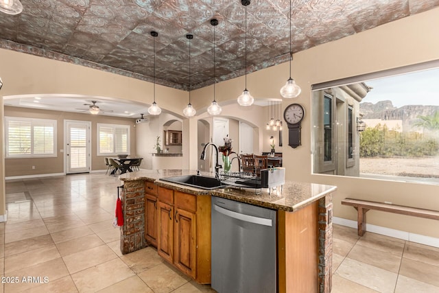 kitchen with a sink, arched walkways, stainless steel dishwasher, and brown cabinets