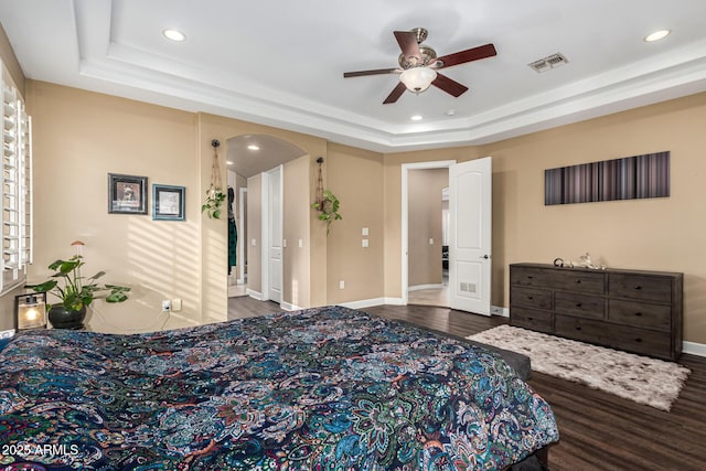 bedroom with a raised ceiling, arched walkways, wood finished floors, and visible vents