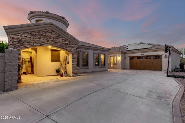 mediterranean / spanish-style house featuring stucco siding, roof mounted solar panels, a tiled roof, an attached garage, and driveway