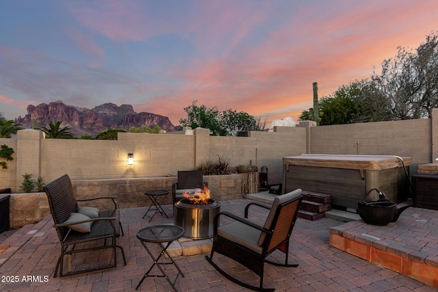 view of patio featuring a fenced backyard, a mountain view, a hot tub, and an outdoor fire pit
