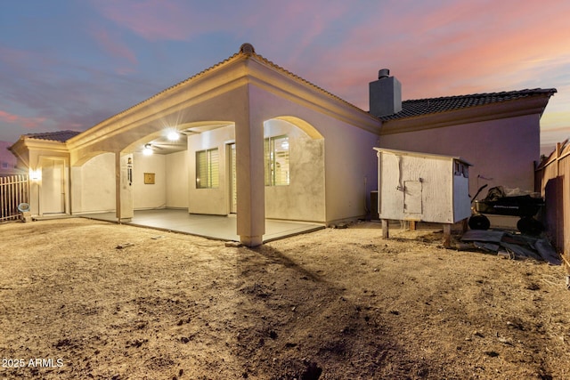 rear view of property featuring fence, stucco siding, a chimney, a patio, and a tiled roof