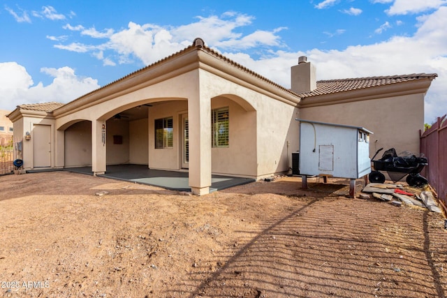 back of house with a chimney, a tile roof, a patio area, fence, and stucco siding