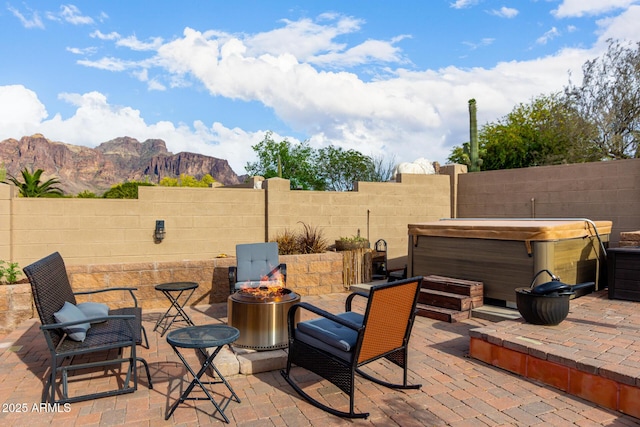 view of patio / terrace with a fenced backyard, a mountain view, a hot tub, and an outdoor fire pit